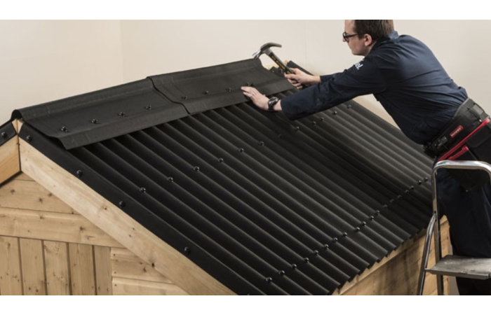 man with hammer fitting black corrugated bitumen sheets to a timber shed