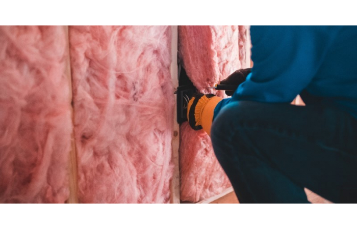 man installing pink loft insulation between joists