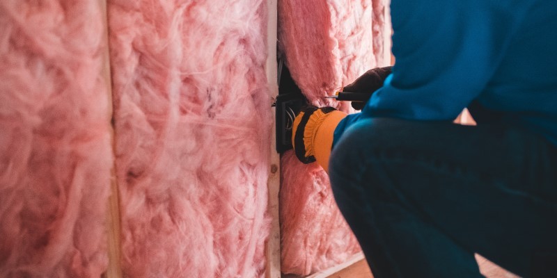 man installing pink loft insulation between joists