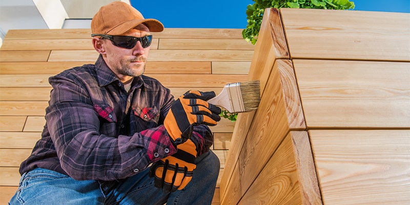 man painting wooden decking with brush